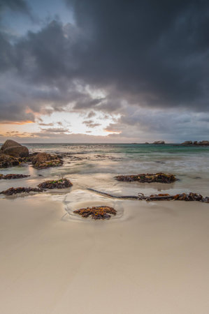Long exposure photography of waves crashing over rocks at sunrise with storm clouds buildingの写真素材