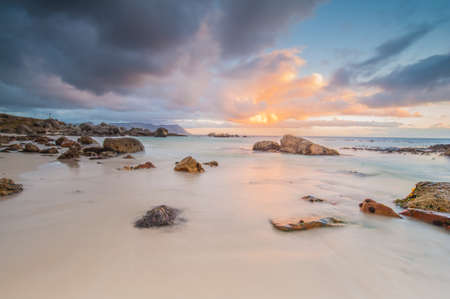 Long exposure photography of waves crashing over rocks at sunrise with storm clouds buildingの写真素材