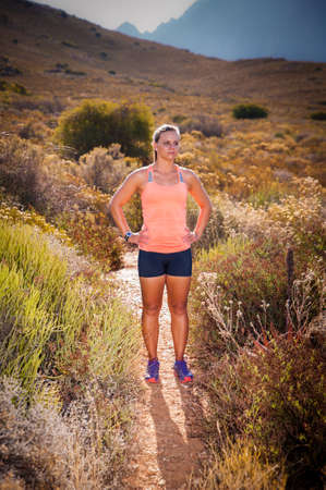 Vibrant image of an athletic looking blonde female trail runner running along an unseen mountain path at sunsetの写真素材