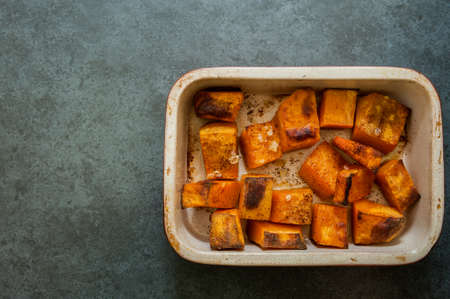 Roasted pumpkin in a ceramic pot on a black slate backgroundの写真素材