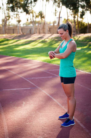 A female athlete at a running track adjusts her heart rate monitor before a workout