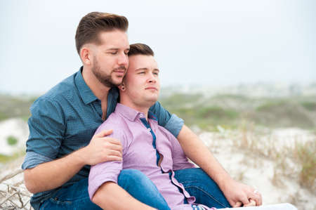 gay men lovingly embracing and cuddling on a beachの写真素材