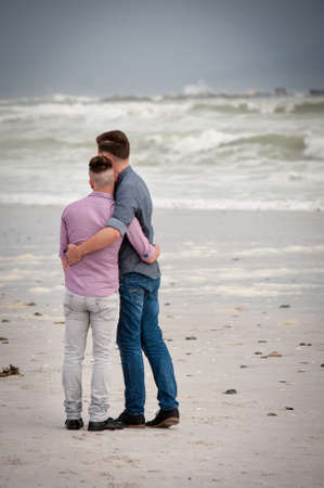 gay men lovingly embracing and cuddling on a beachの写真素材