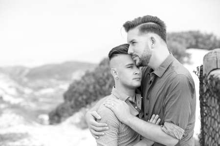 two gay men lovingly embrace and kiss next to a beach fenceの写真素材
