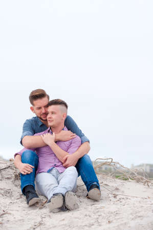 gay men lovingly embracing and cuddling on a beachの写真素材