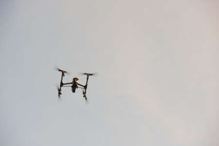 Close up of an aerial drone flying overhead filming aerial footage. UAV in action against a blue sky backgroundの写真素材