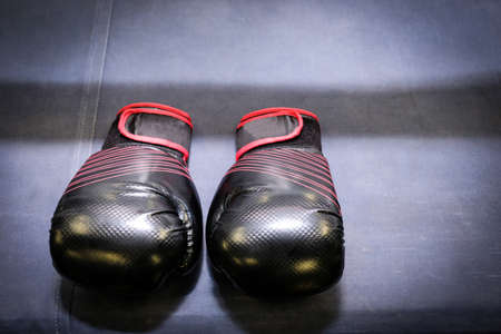 black and red boxing gloves laid on the edge of a boxing ring