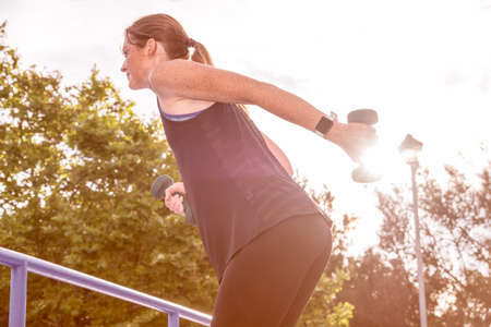 warm and vibrant image of a female working out using dumbbells in a street scene at sunriseの写真素材