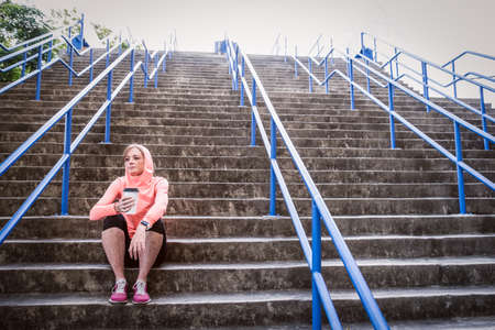 image of a female athlete sitting on stairs and having a post workout recovery drinkの写真素材