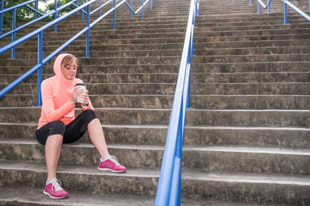 image of a female athlete sitting on stairs and having a post workout recovery drink