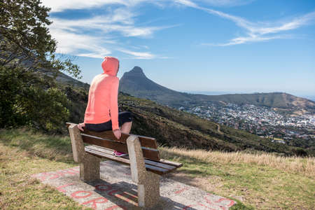 attractive mid thirties female wearing sports clothing sat on a bench over looking cape town south africaの写真素材