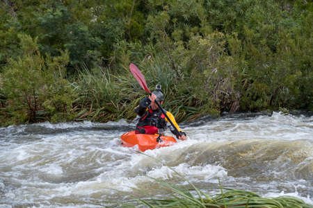 Image of a kayaker in an orange kayak padding through some white water rapids on a river in Du Toits Kloof near Cape Town South Africaの写真素材