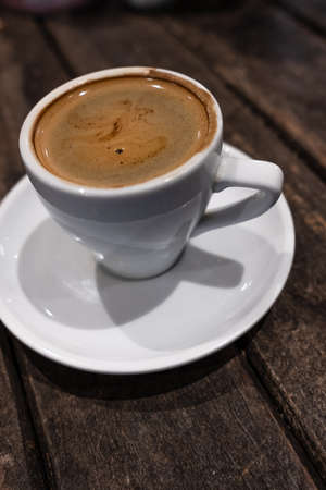 double espresso served in a white cup and saucer on a dark wooden table in a cafeの写真素材