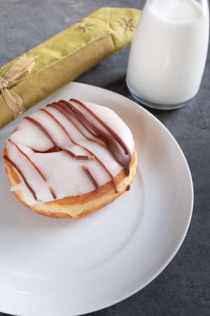 white iced ring doughnut on a white plate with milk, a napkin and slate backgroundの写真素材