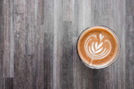 latte coffee with attractive pattern in a glass cup on a wooden tableの写真素材