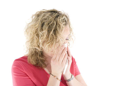 Young blond girl sneezing in the handkerchief in front of the white background の写真素材