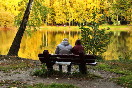 Two people on bench near lake in autumn day, September 28, 2014, Moscow, Russiaの写真素材