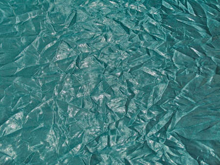 Texture of shiny fabric with creased folds in turquoise color
