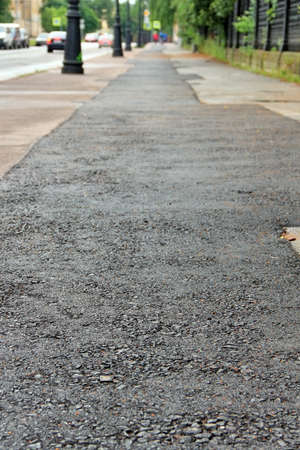 Neatly repaired asphalt on pedestrian pavement in city. Shallow depth of field. Focus on bottom of frame, view of city in blurの写真素材