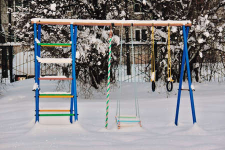 Baby swings in snow in city park in deep winter