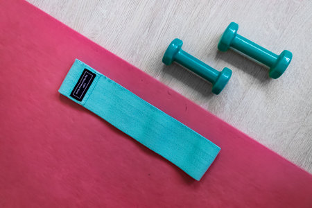 Turquoise dumbbells and elastic band for fitness on pink yoga mat.