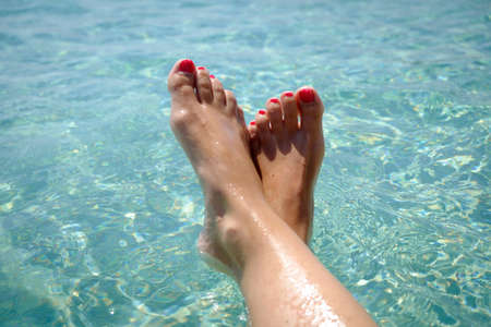 Feet with red pedicure of girl on the background of sea. Girl at the resort. Female feet on sea background. Girl sunbathes on a beach. Meditation on the sea.の写真素材