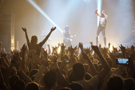 Concert shot, a huge crowd is standing in front of a lit stage clapping a band performance.の写真素材