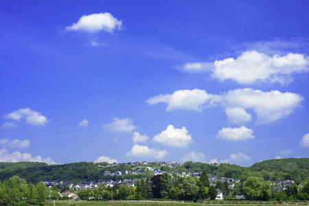 An image of a village in Germany from across the river rhein with a low horizon and a deep blue sky scattered with fluffy white cloudsの写真素材