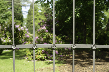 An image of a flower garden protected by an iron fence with crafted handiworkの写真素材