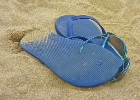Thongs and a pair of glasses in the sand の写真素材