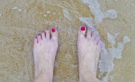 Close up of womanfoots with red nails polish in the water of a the beachの写真素材
