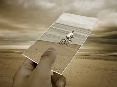 Concept creative collage with a hand holding a photo of an old man biking  and a nice isolated beach in the backgroundの写真素材