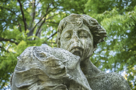 Unique low angle view of a couple about to kiss gray sculpture in blurred trees and plants background taken in botanical garden of Montevideo, Uruguay.の写真素材