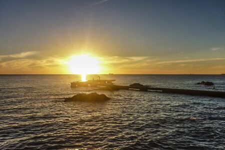 Beautiful sunset scene of the sea with silhouettes people at the breakwater in the city of Montevideo, Uruguay.の写真素材