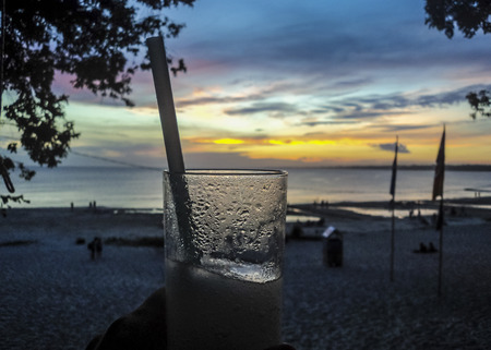 Beautiful aerial view of sunset at the beach with a hand holding a drink as the main subject and shore and sky at background.の写真素材