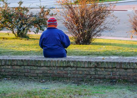 Back view of older woman wearing winter clothes sitting at park in Montevideo, Uruguay.の写真素材