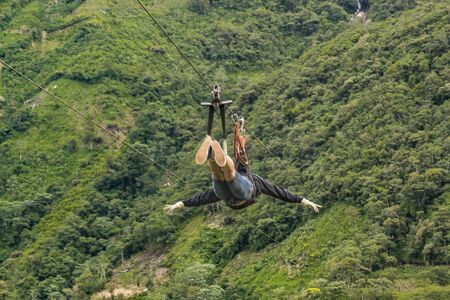 Person making canopy, and extreme touristic activity hanged on wire at highs in Banos, Ecuadorの写真素材