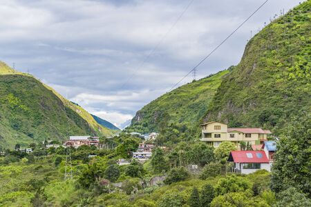 Aerial view of a group of houses and buildings located in valley surrounded by leafy mountains in Banos, Ecuadorの写真素材
