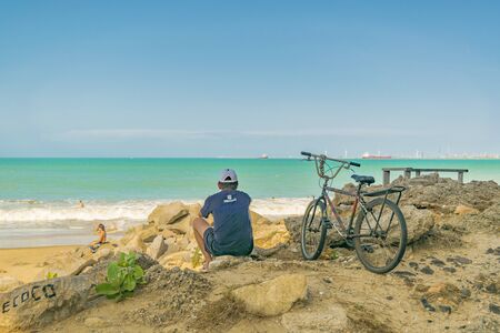 FORTALEZA, BRAZIL, DECEMBER - 2015 - Back view of adult man sitting on rock watching the beach in Fortaleza, Brazilのeditorial素材