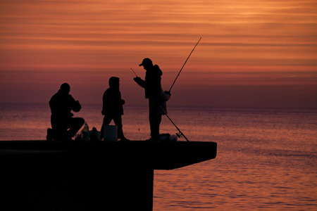 High contrast photo of group of people fishing at breakwater at coast of river in Montevideo city, Uruguayの写真素材