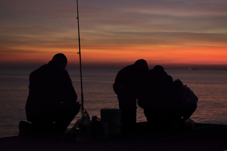 High contrast photo of group of people fishing at breakwater at coast of river in Montevideo city, Uruguayの写真素材
