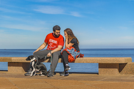 MONTEVIDEO, URUGUAY, AUGUST - 2017 - Young couple with pet sitting at boardwalk at Montevideo city, Uruguayのeditorial素材