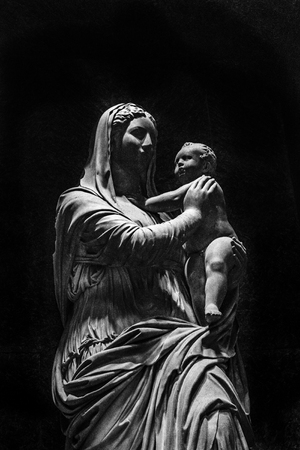 High contrast classical style sculpture decpicting a woman with baby in hands over black background
