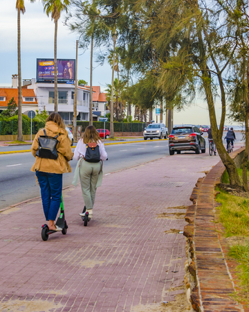 MONTEVIDEO, URUGUAY, MAY - 2019 - Two women friends riding electric skateboard at sidewalk, montevideo, uruguayのeditorial素材