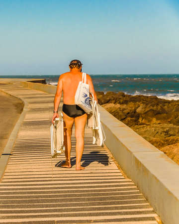 PUNTA DEL ESTE, URUGUAY, FEBRUARY - 2020 -  Summer scene senior man with beach clothes walking at boardwalk, punta del este city, Uruguayのeditorial素材