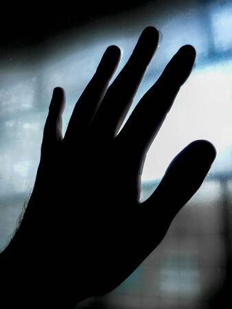 High contrast photo left hand touching blurred window glassの写真素材