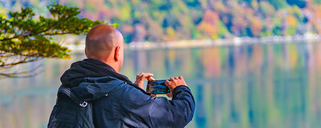 Adult man taking photos with smartphone at border of lake, ushuaia, tierra del fuego, argentinaの写真素材