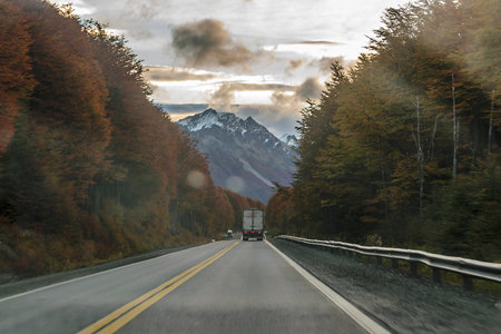Cargo truck crossing highway surrounded by forest landscape, Tierra del Fuego province, Argentinaの写真素材