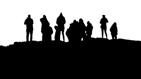 Black graphic silhouette of a group of people standing at the top of rocky hillの写真素材