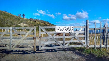 Meadow landscape scene with wooden fence with spanish text signpost do not pass, Tierra del Fuego,...